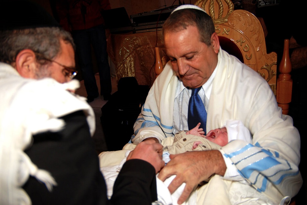 Mohel holding a jewish baby boy for brit milah ceremony