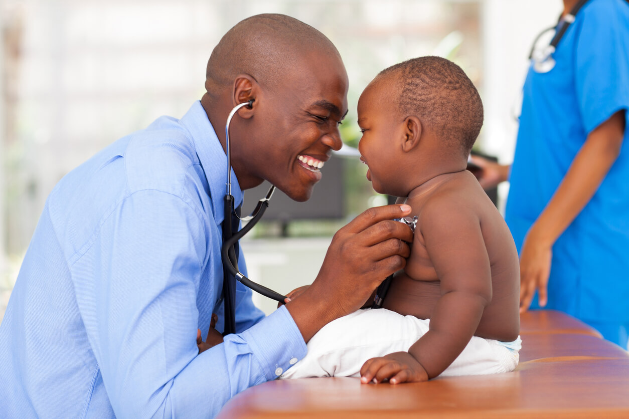 Happy African Male Doctor Examining Baby Boy With Female Nurse on Background