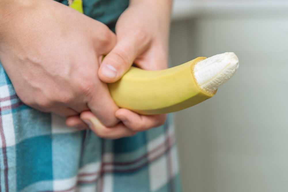 Hand of a Young Man With a Banana With the Tip of Its Skin Removed Depicting a Circumcised Male Member