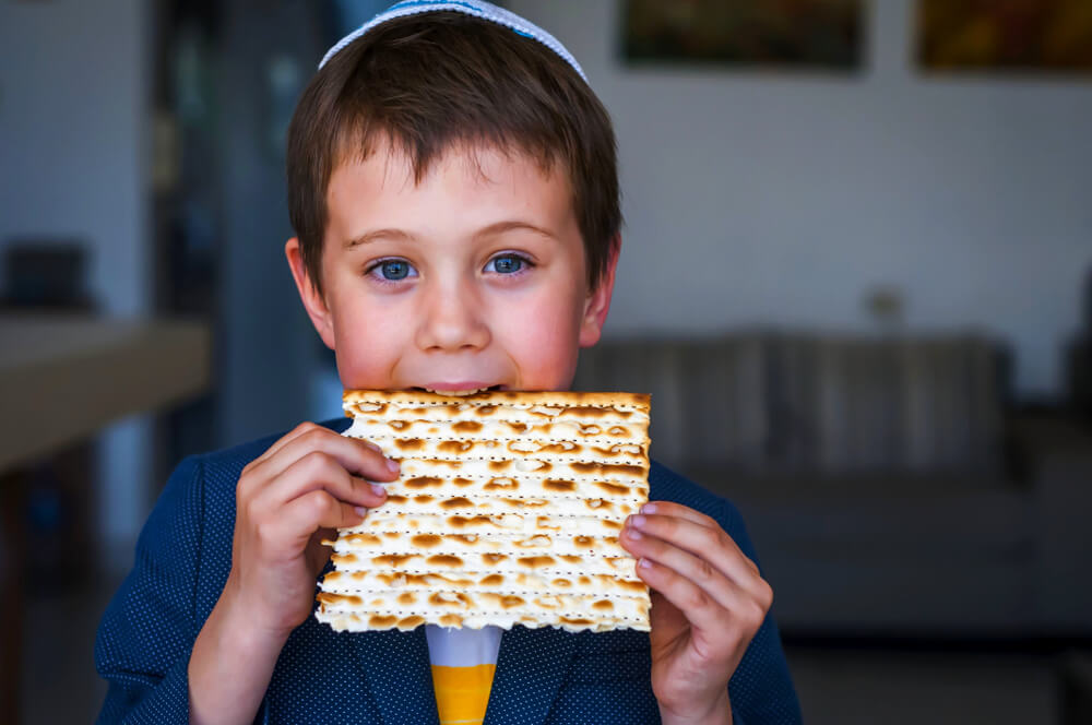 Cute Caucasian Jewish Boy Holding in His Hands and Taking a Bite From a Traditional Jewish Matzo Unleavened Bread. 