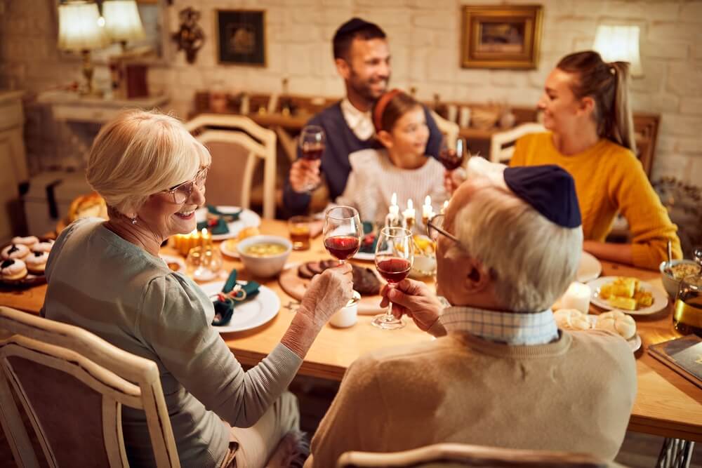 Happy Senior Jewish Couple Toasting With Wine During Family Dinner on Hanukkah.