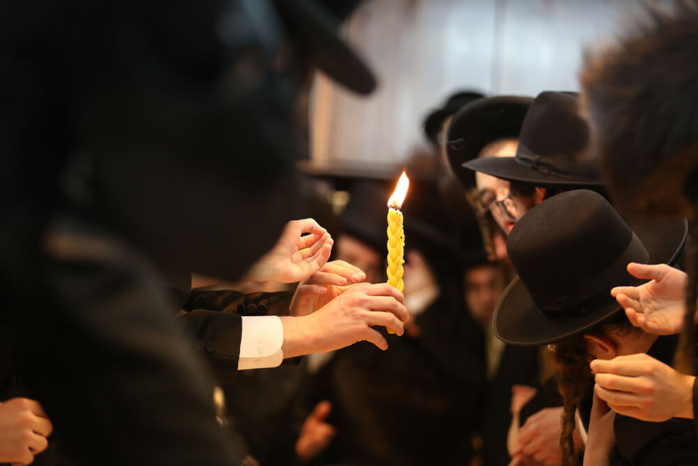 Orthodox Religious Hasidic Jews Extend Their Hands to the Light of the “Havdalah” Candle