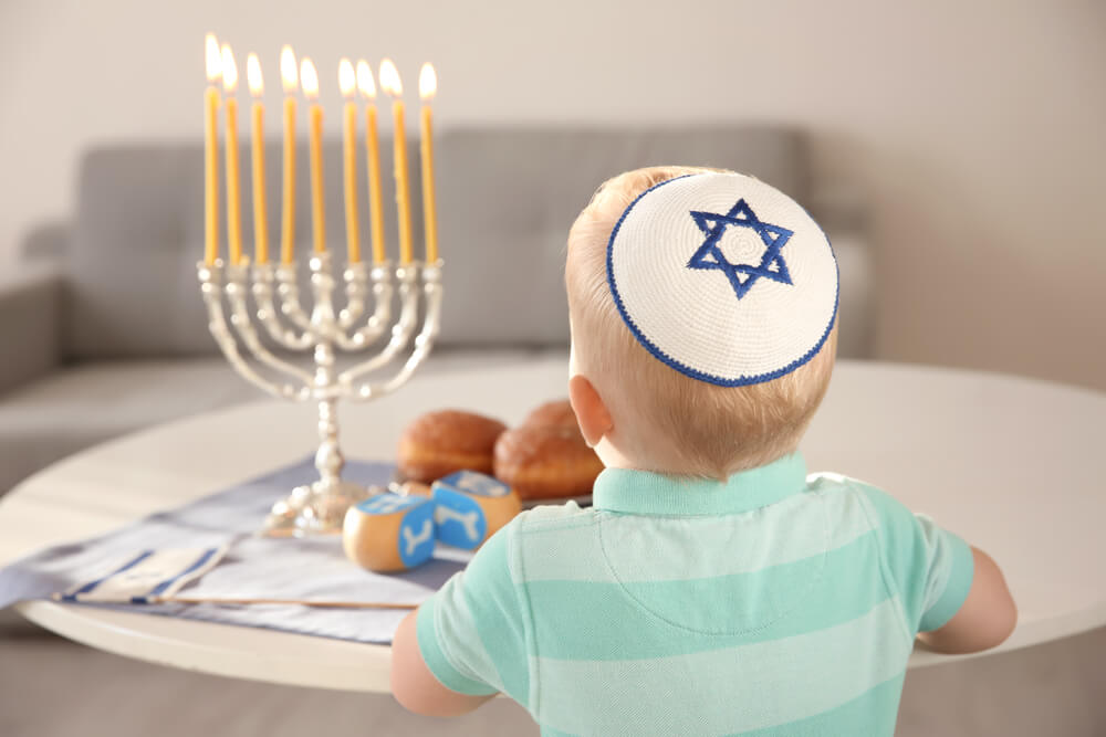 Cute Boy Sitting Near Nine branched Menorah on Table at Home