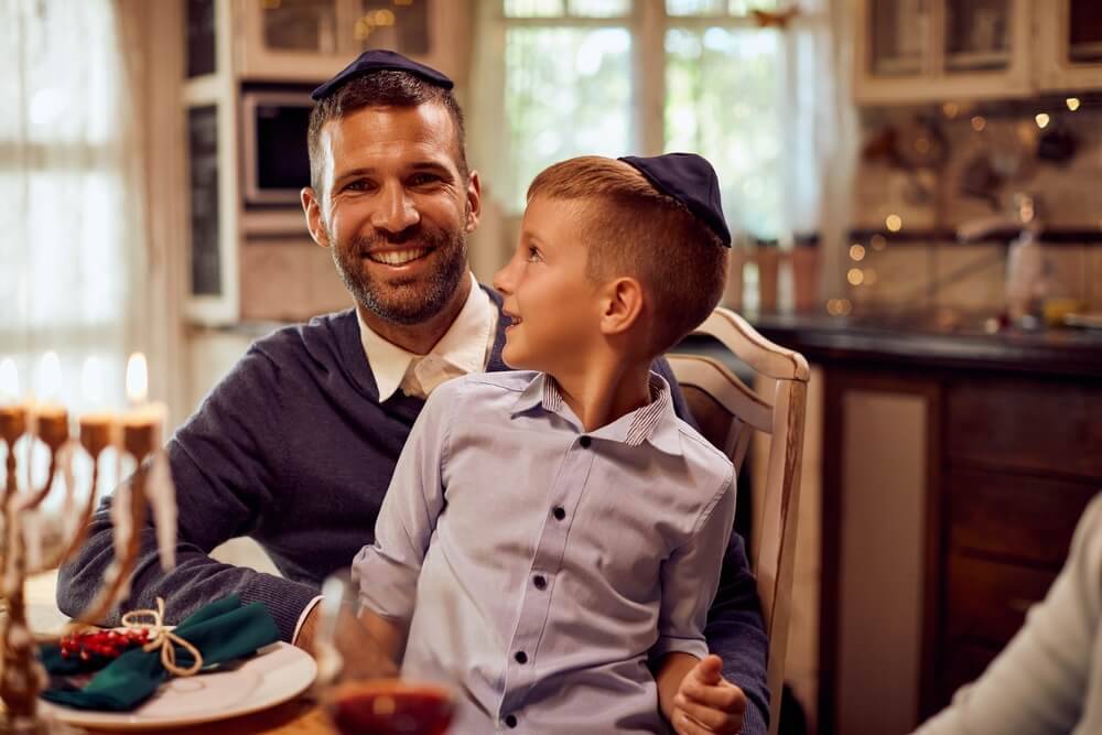 Happy Father and Son Wearing Yarmulke While Celebrating Hanukkah at Dining Table at Home