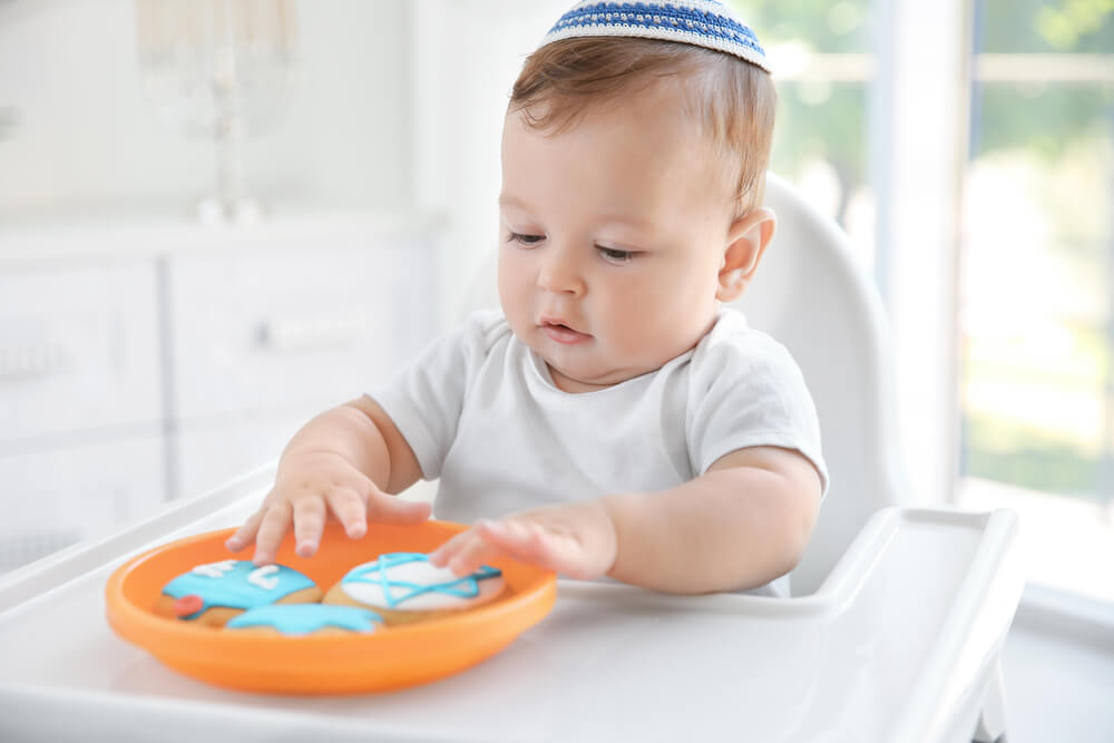 Cute Baby Eating Festive Cookies While Sitting on High Chair