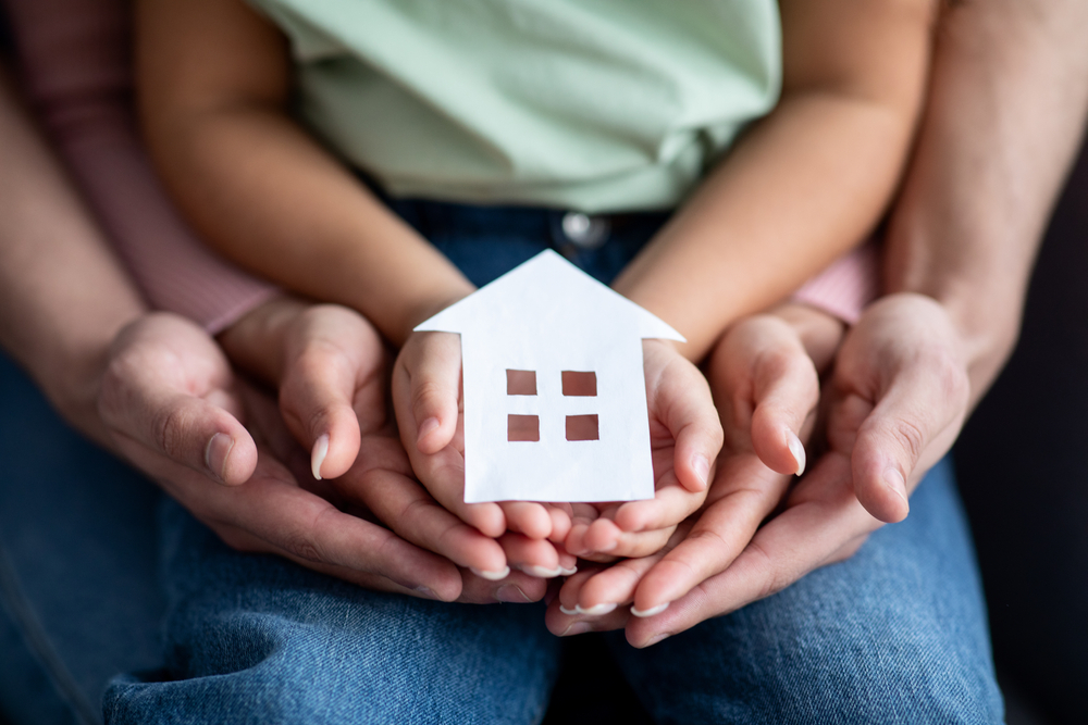 Man Woman and Little Child Holding Cutout Paper House Figure in Hands